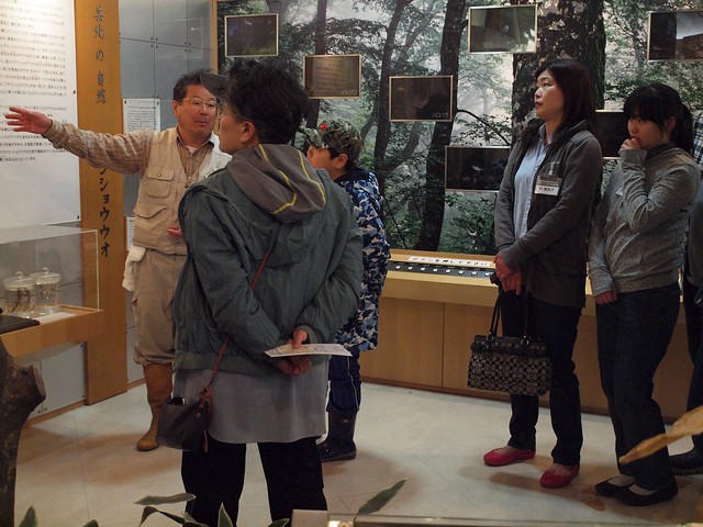自然館の中で、サンショウウオについて説明する内藤先生と、真剣に聞き入る参加者さんたち。